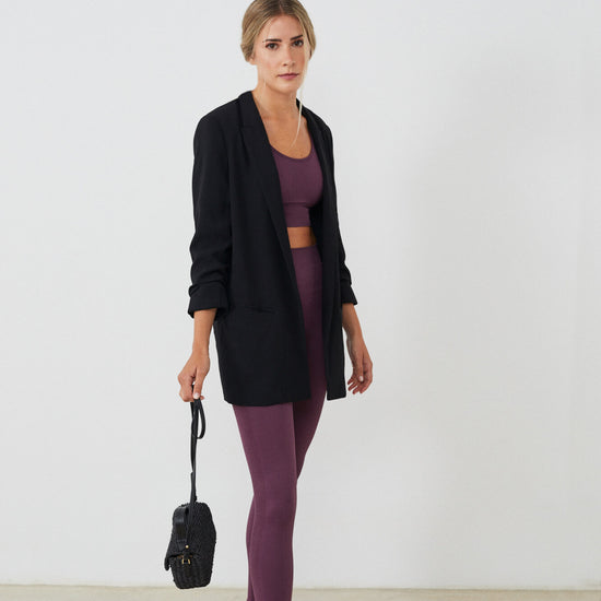 Conjunto yoga mujer marca NOY (not only yoga) modelo GAIA y top AINE con volantes sin costuras tono cereza pansy plum combinado con chaqueta negra bolso y sandalias negras