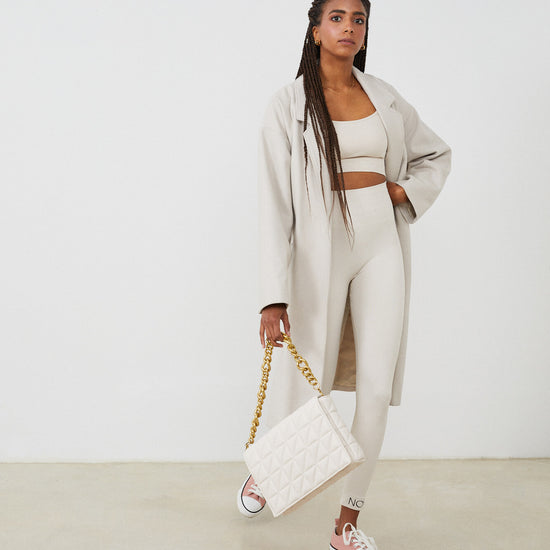 Conjunto yoga mujer marca NOY (not only yoga) modelo GAIA y top SELENE sin costuras con tirantes tono nude sand combinado con abrigo blanco largo bolso y converse rosas