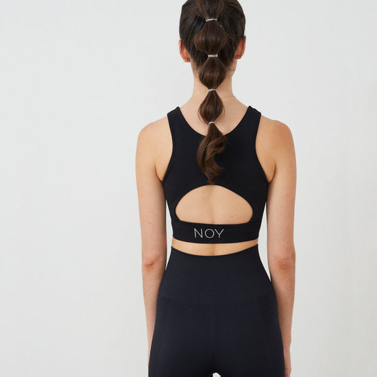 Vista trasera top yoga mujer marca NOY (not only yoga) modelo HERA con apertura bajo pecho y espalda tono negro black lava